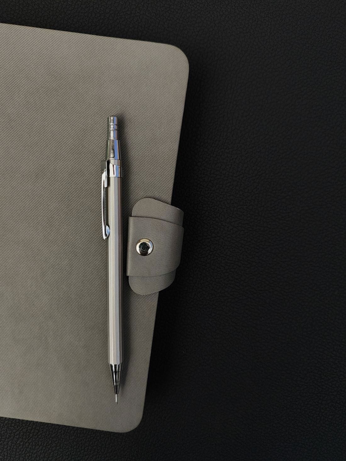 A pencil lying on a grey leather notebook, on a dark leather desk.